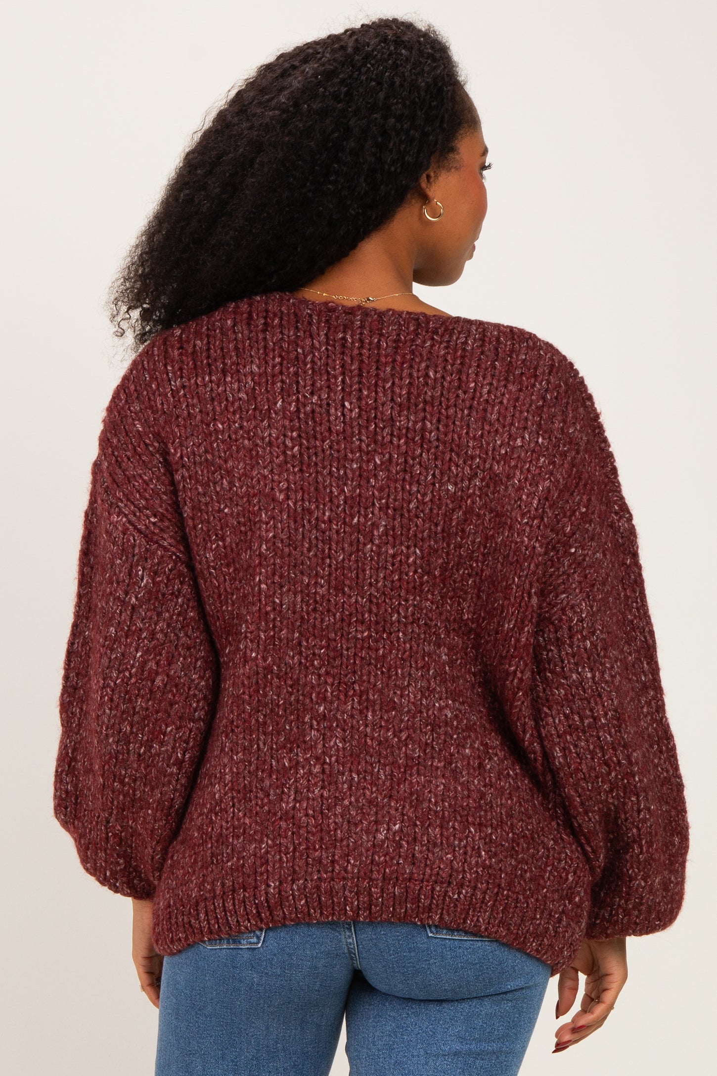 woman wearing a burgundy oversized knit sweater with balloon sleeves and styled with blue jeans, viewed from the back