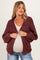 woman wearing a maroon chunky knit maternity cardigan over a beige top and showing her baby bump
