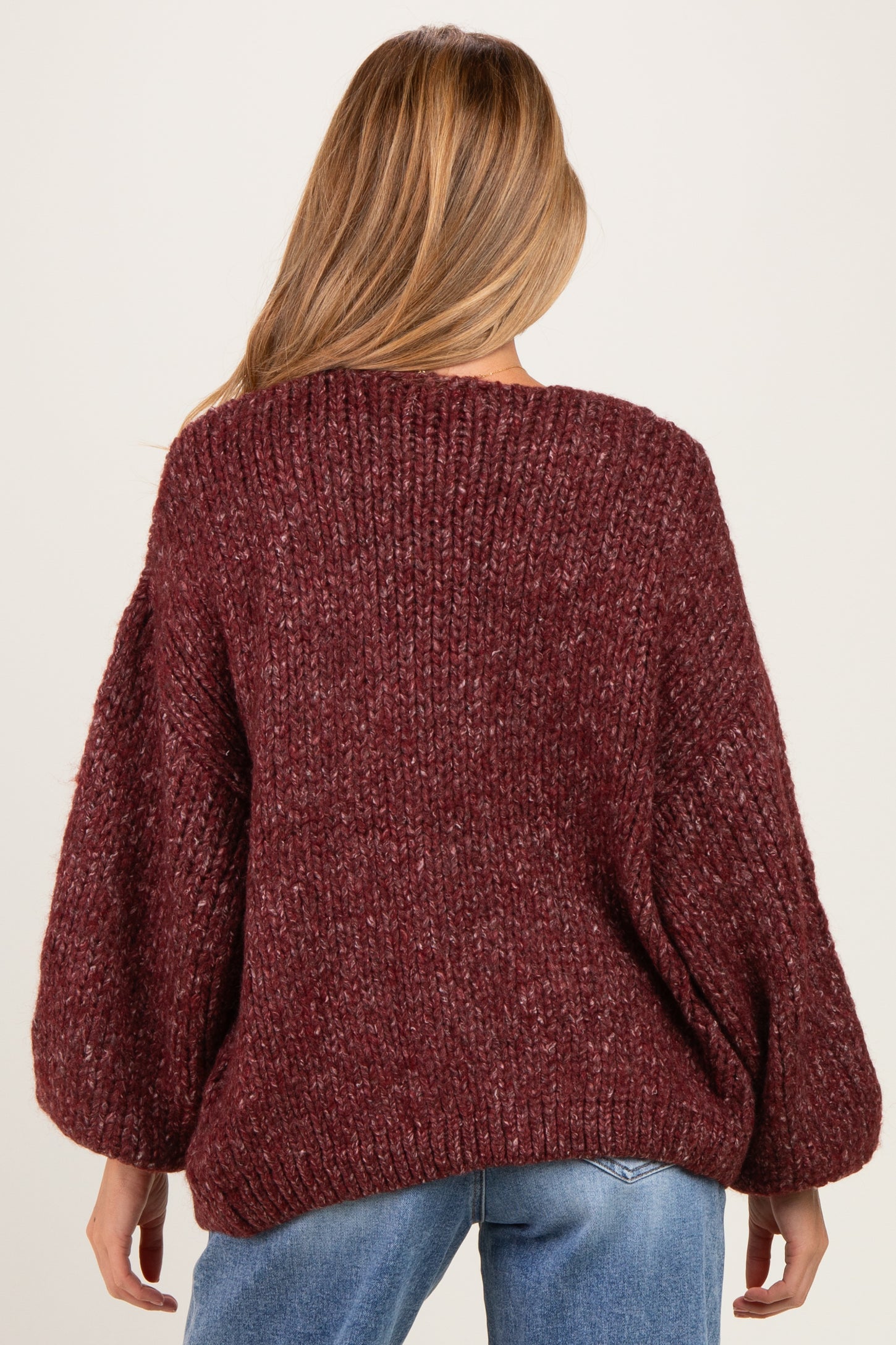 woman wearing a burgundy chunky knit maternity sweater with balloon sleeves, seen from the back