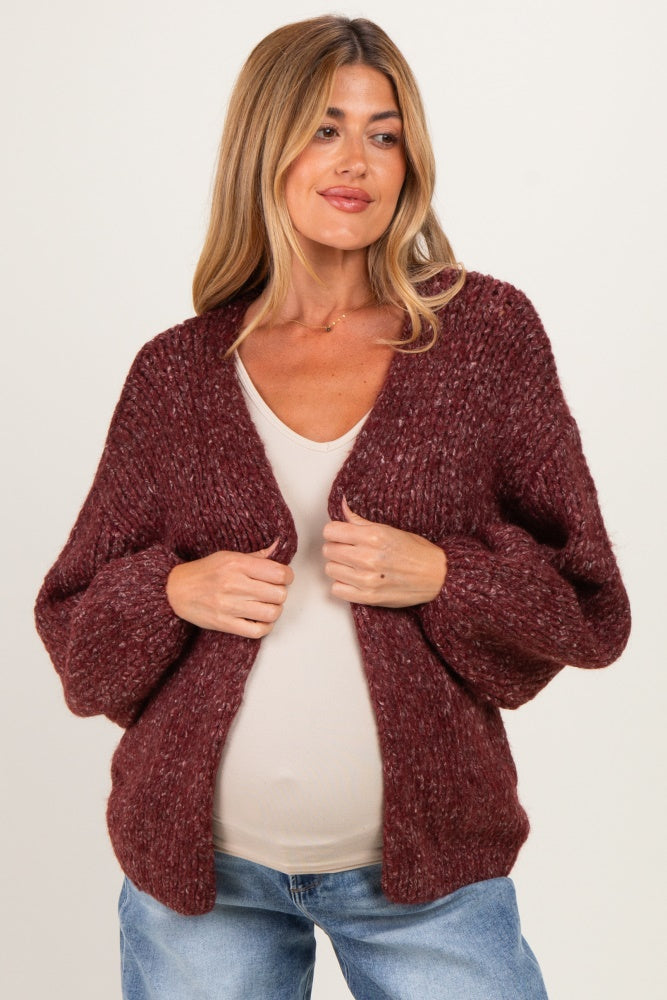 woman wearing a maroon chunky knit maternity cardigan over a beige top and showing her baby bump