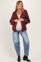 woman wearing a burgundy chunky knit maternity cardigan over a beige top and blue jeans, showing her baby bump