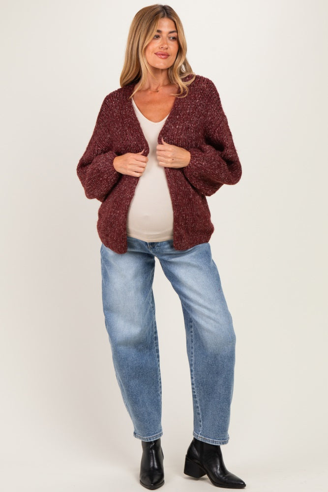 woman wearing a burgundy chunky knit maternity cardigan over a beige top and blue jeans, showing her baby bump