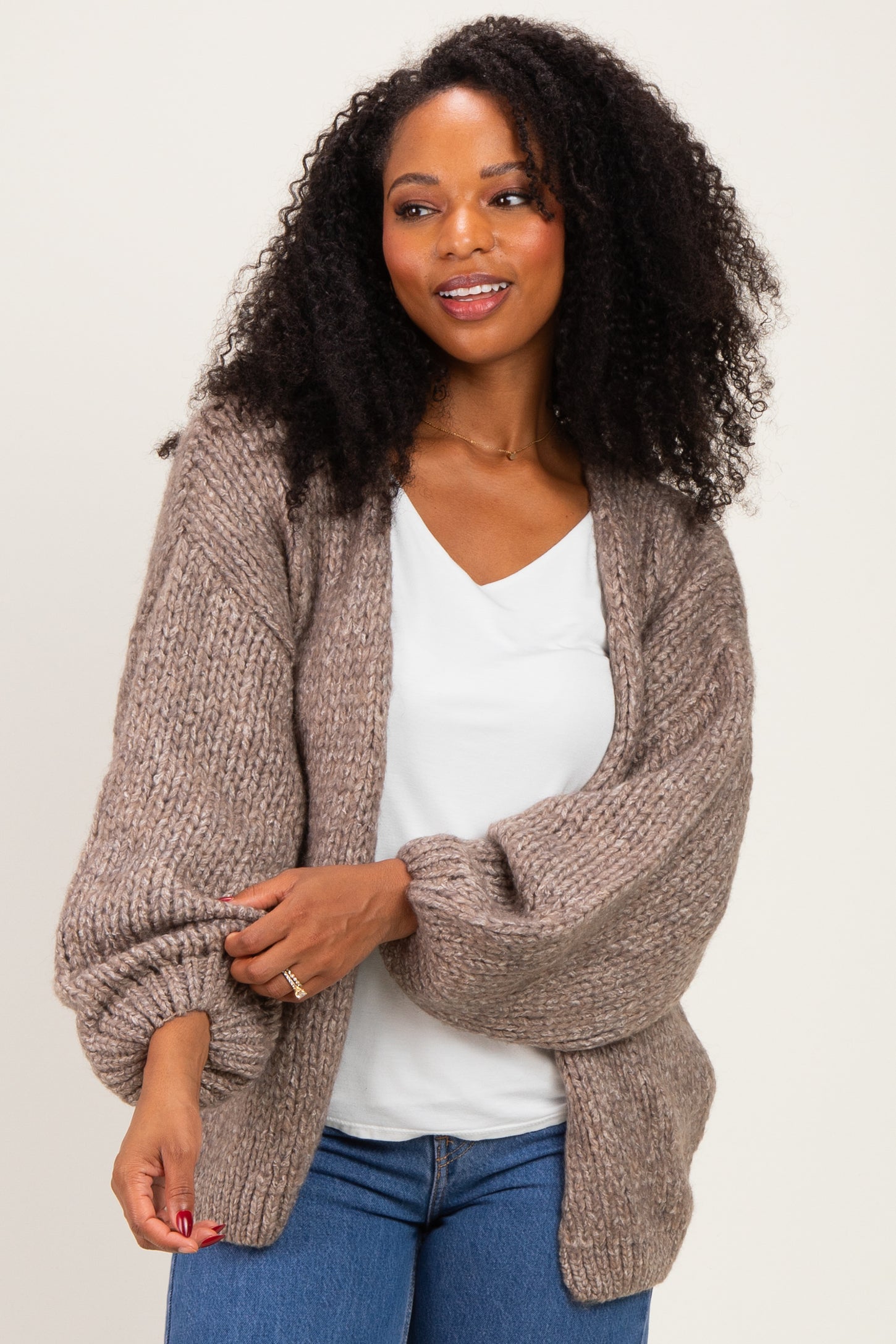 woman wearing a tan oversized knitted cardigan over a white top with blue jeans and curly hair