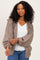 woman wearing a tan oversized knitted cardigan over a white top with blue jeans and curly hair