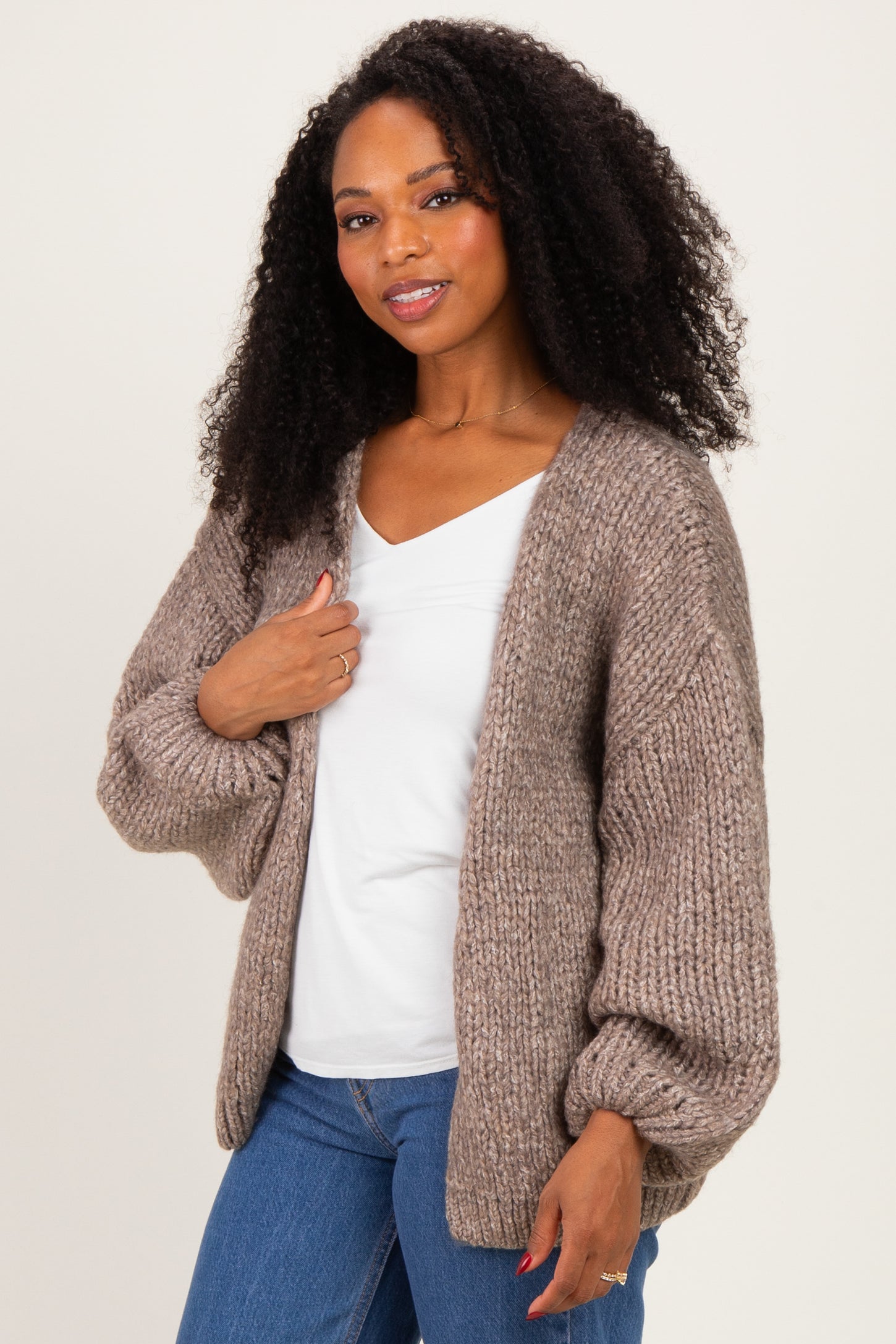 woman wearing a cozy oversized taupe knit cardigan over a white v-neck top and blue jeans