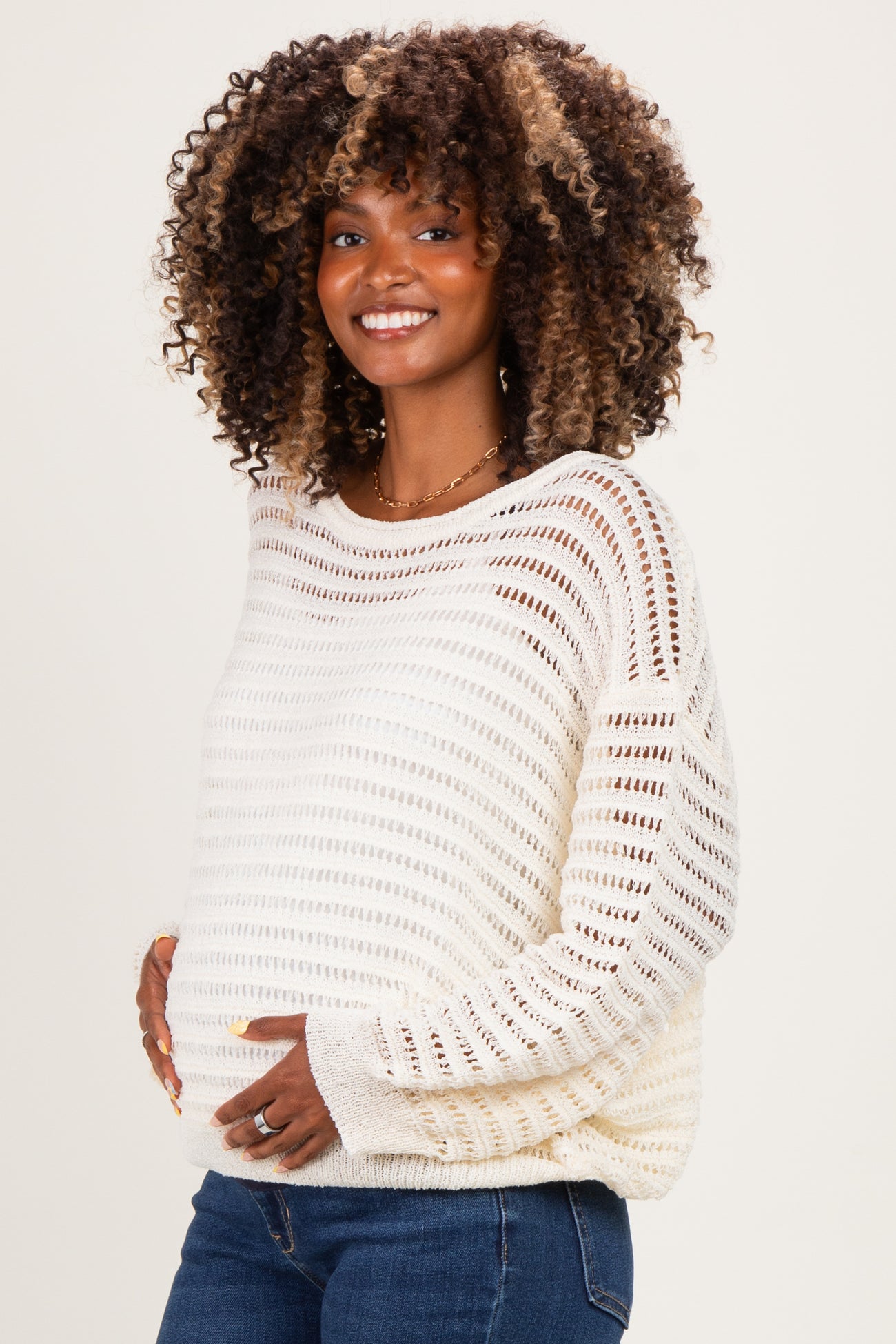 woman wearing a cream open knit maternity sweater and showing her baby bump