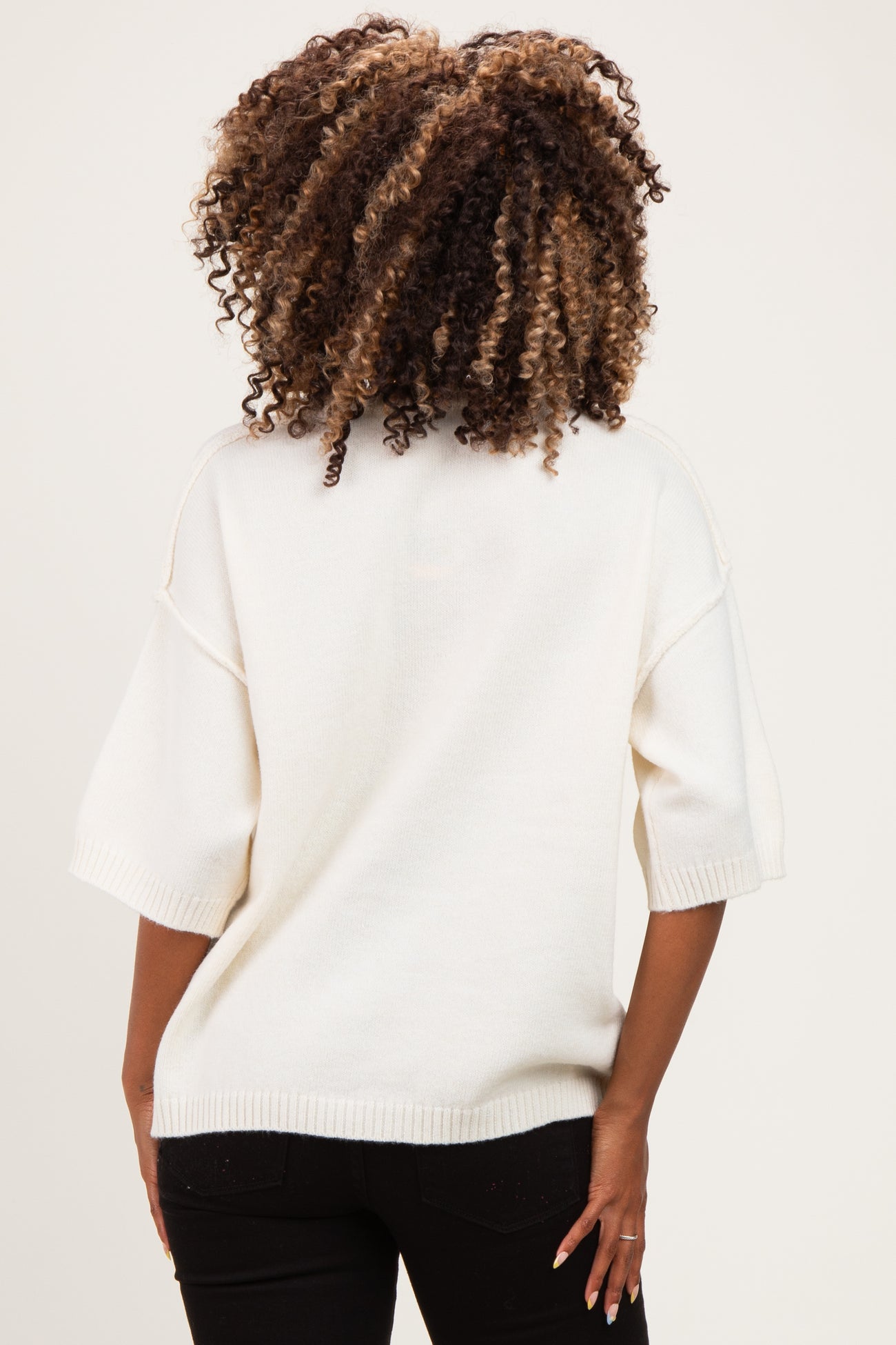 woman wearing a white oversized maternity sweater, visible from the back with curly hair and relaxed fit design