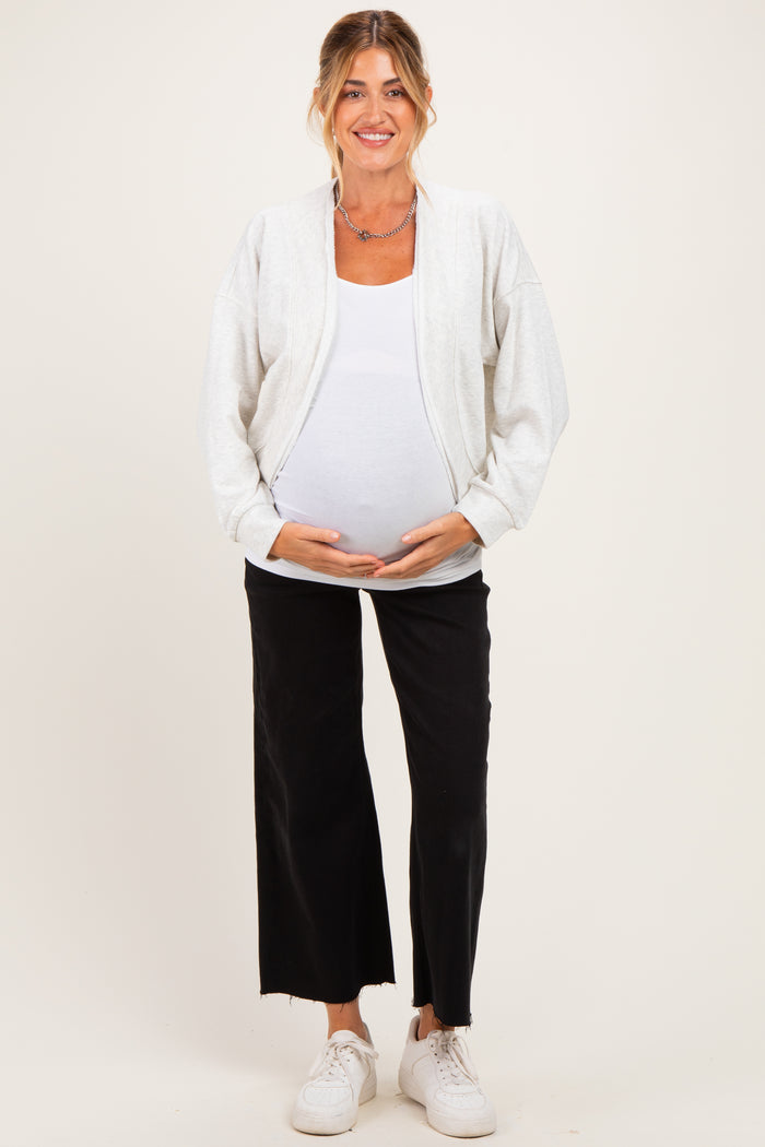 woman wearing a light gray maternity zip-up jacket over a white tank top and black wide-leg pants, showing her baby bump