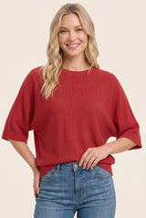 woman wearing a red oversized knit sweater and blue high-waisted jeans, smiling at the camera