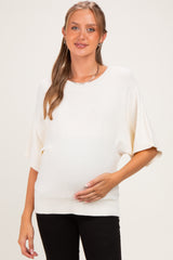 woman wearing a cream oversized maternity sweater and gently cradling her baby bump