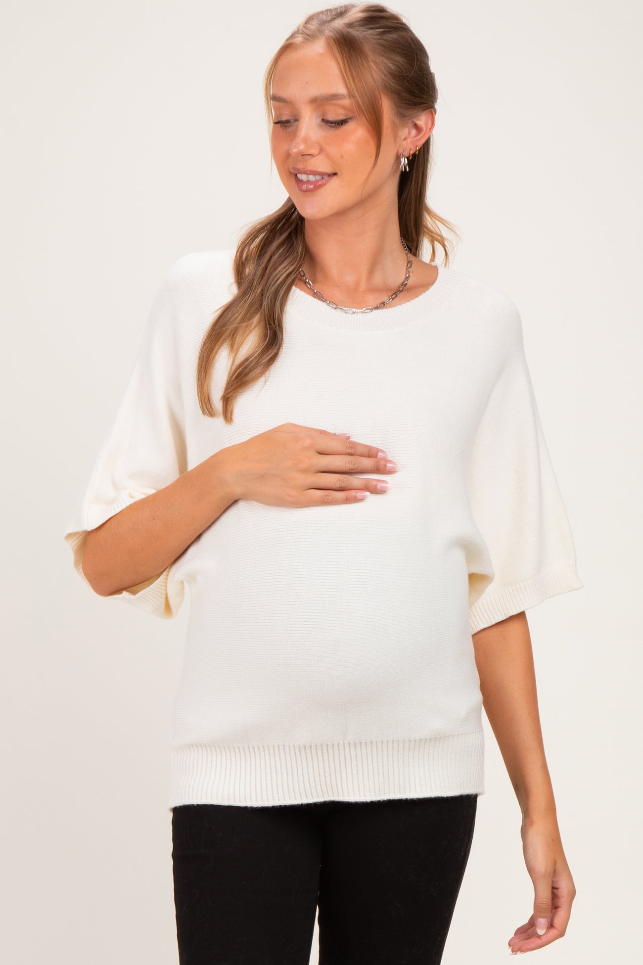 woman wearing a cream short sleeve maternity sweater and cradling her baby bump