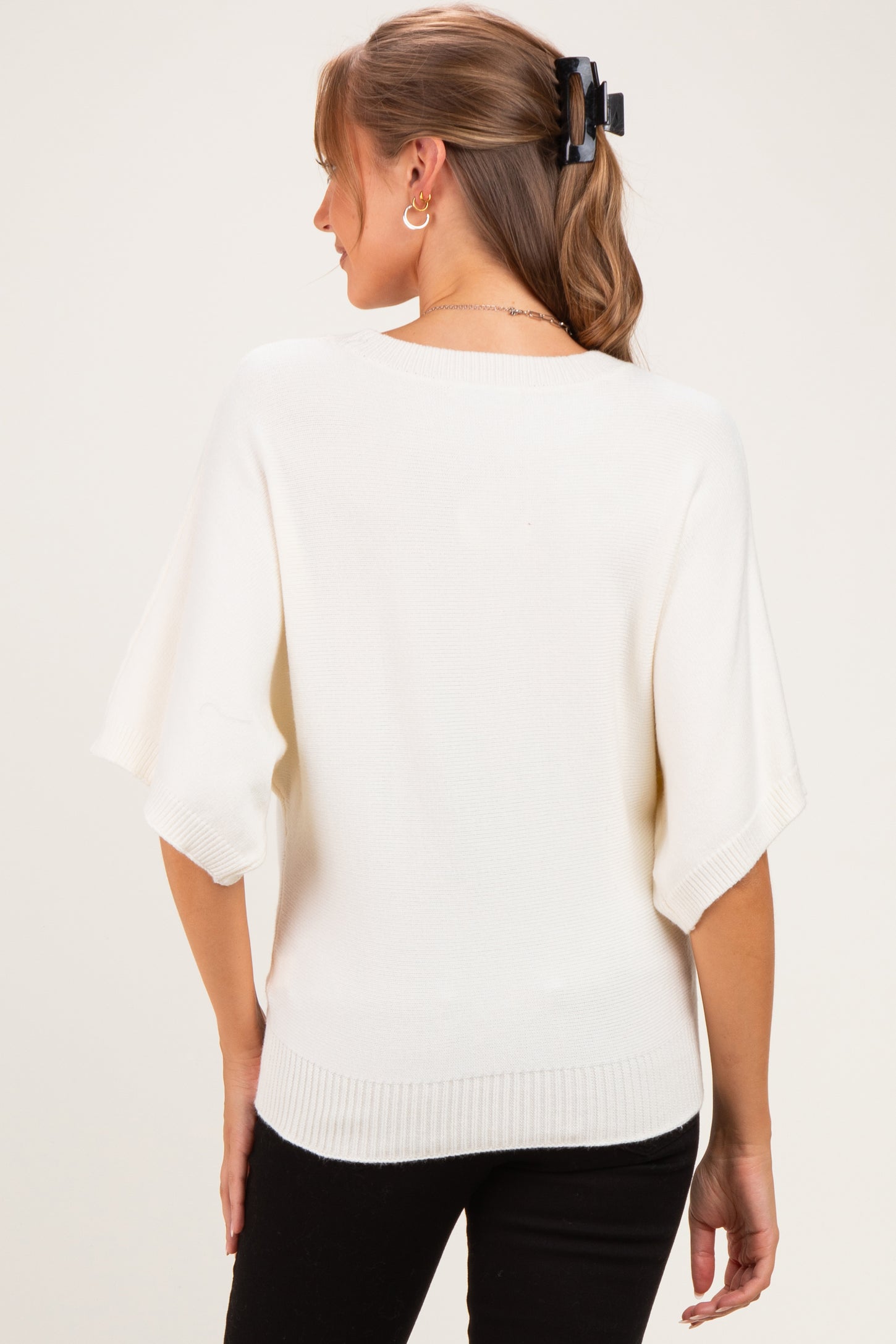 woman wearing a cream oversized maternity sweater with short sleeves and a round neckline, showing the back view