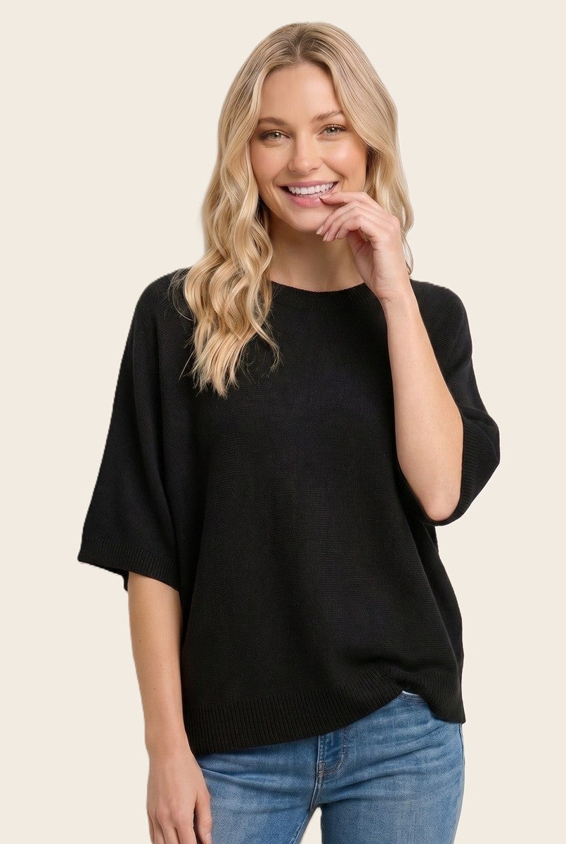woman wearing a black oversized knit sweater and smiling with casual blue jeans