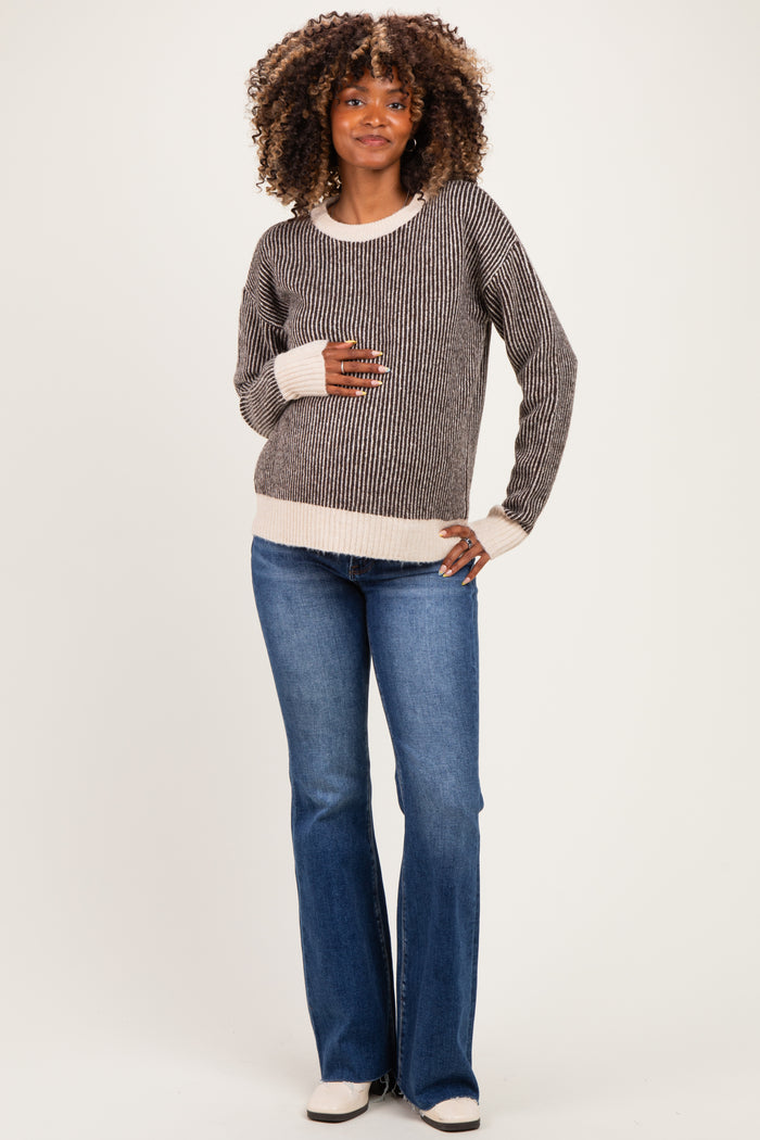 woman wearing a striped maternity sweater with a light cream hem and blue flared jeans, holding her baby bump