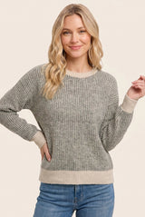 woman wearing a gray striped long sleeve sweater with light beige accents and casual blue jeans