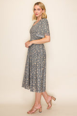 woman wearing a grey floral midi dress with short sleeves and a pleated skirt, paired with nude heeled sandals