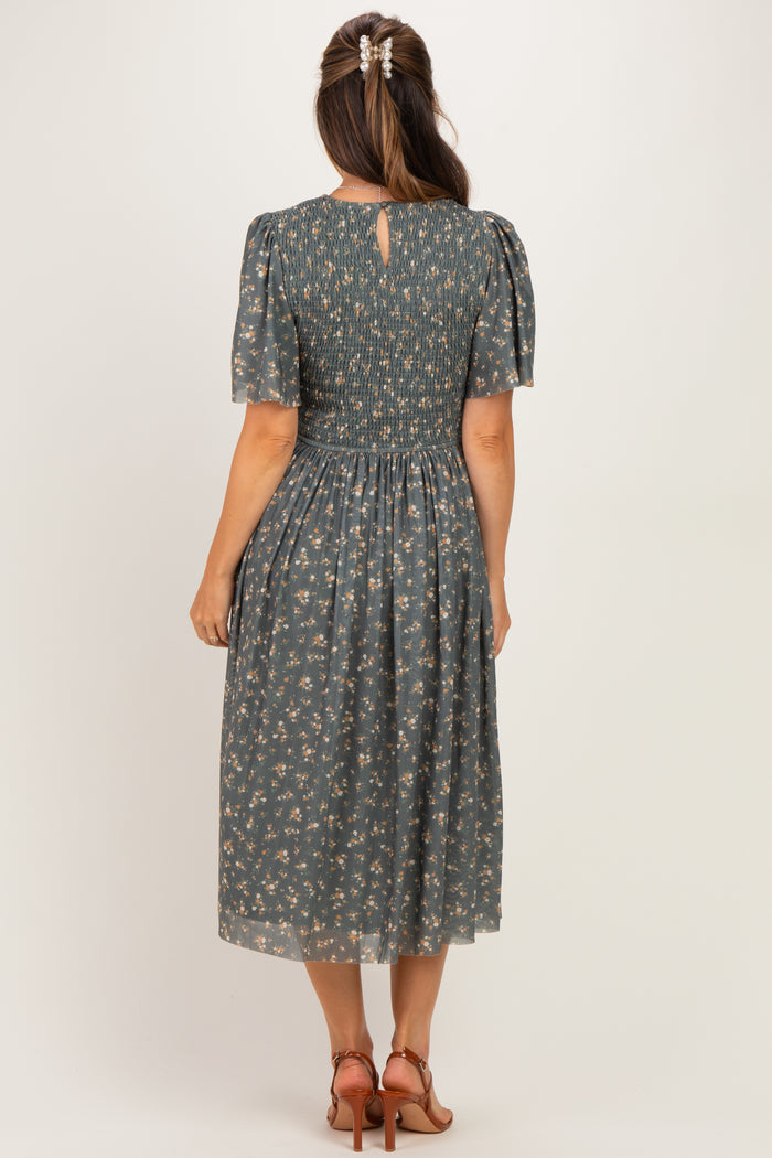 woman wearing a dark green floral maternity dress with short puff sleeves and a smocked back detail