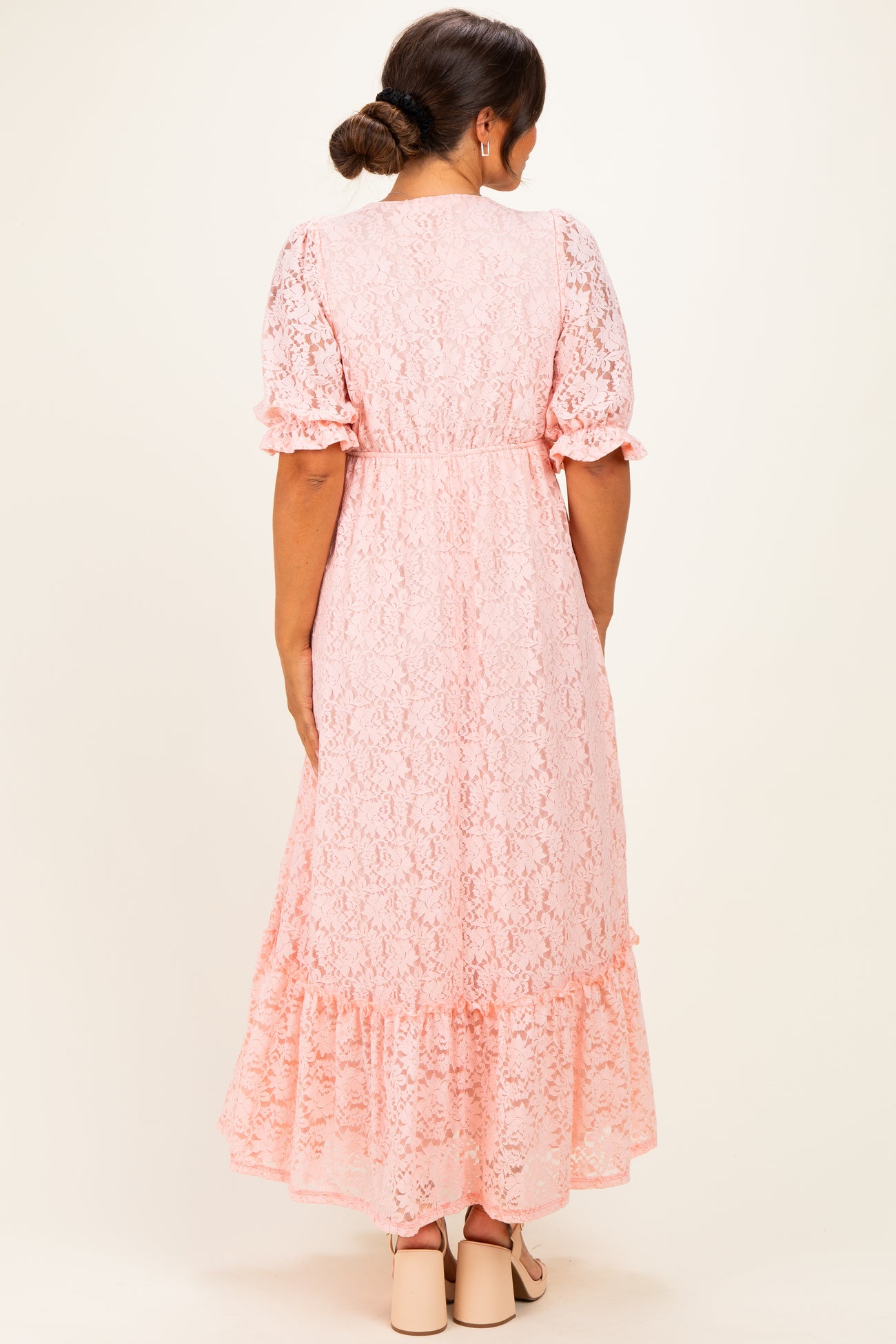 woman wearing a pink lace maternity dress with short puff sleeves and a ruffled hem, showing a baby bump from the back
