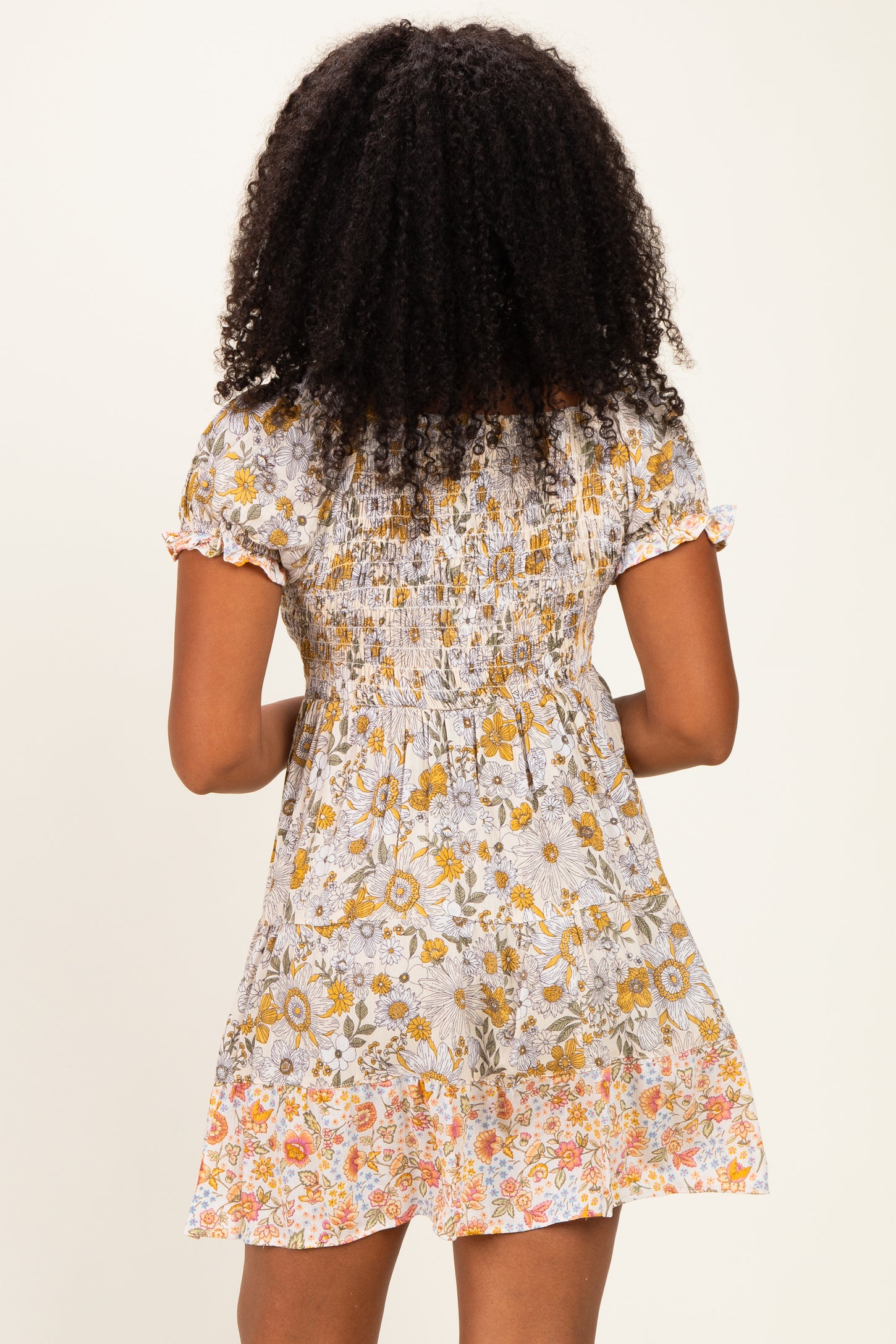 woman wearing a floral print short dress with a shirred bodice and ruffled sleeves, seen from the back