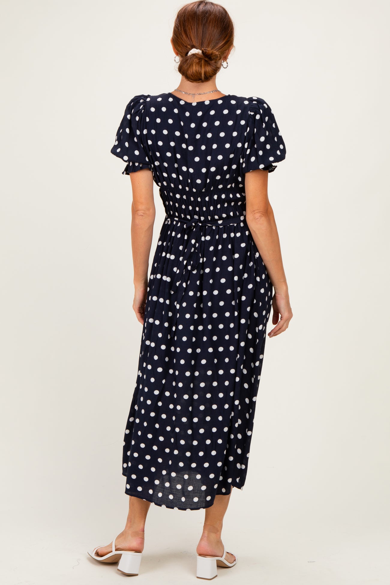 woman wearing a navy blue polka dot midi dress with puff sleeves and a cinched waist, viewed from the back