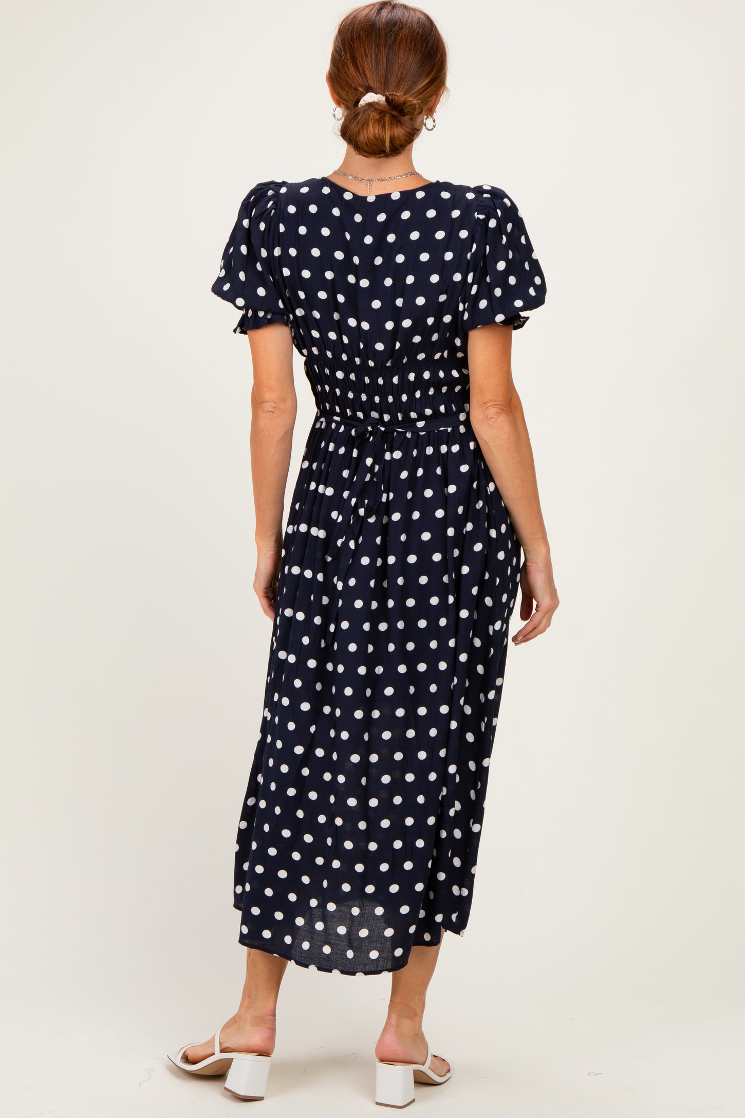 woman wearing a navy blue polka dot midi dress with puff sleeves and a cinched waist, viewed from the back
