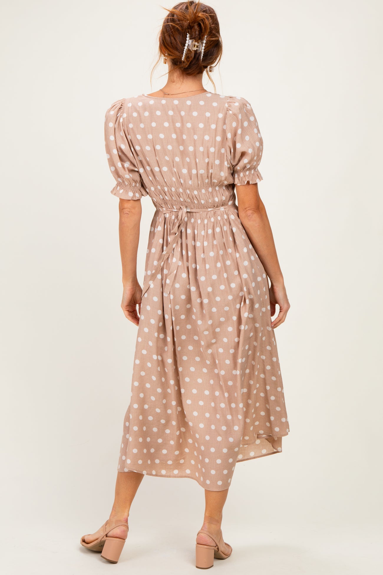 woman wearing a taupe polka dot midi dress with puff sleeves and a cinched waist, view from the back