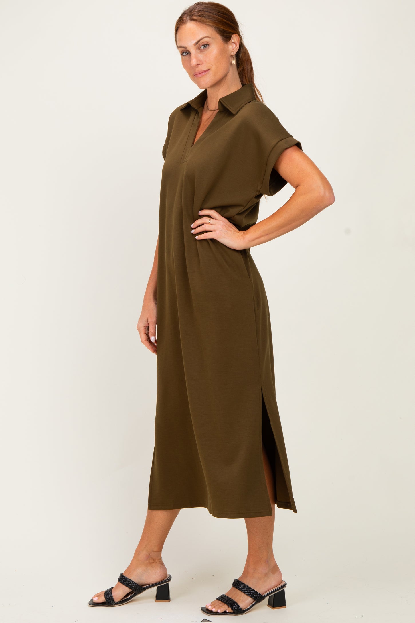 woman wearing an olive green short sleeve midi dress with a collar and side slits, standing in profile
