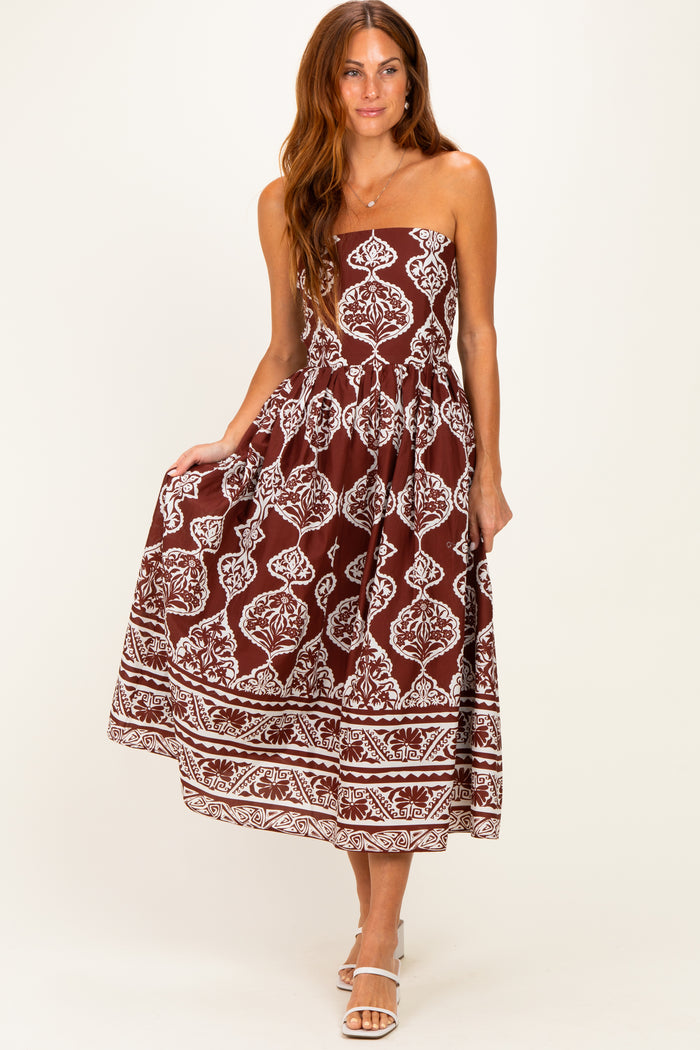 woman wearing a brown spaghetti strap maxi dress with white floral patterns and a tiered skirt