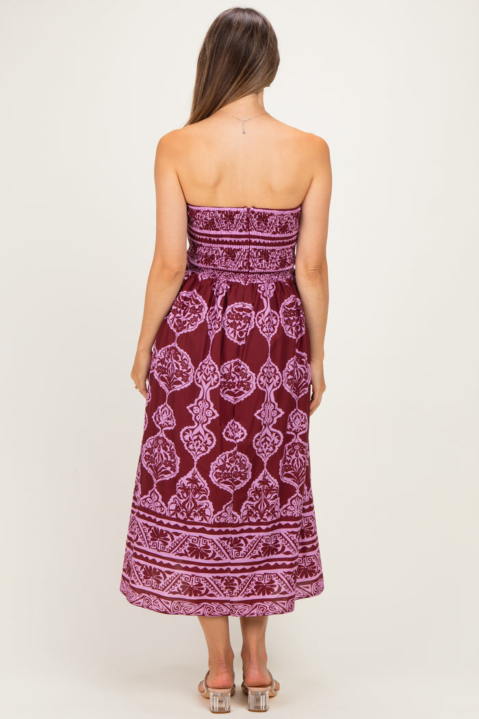 woman wearing a strapless burgundy maternity dress with white fabric pattern, showing her back and flowing mid-calf length