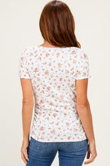 woman wearing a white short sleeve top with a floral print and a fitted silhouette, viewed from the back