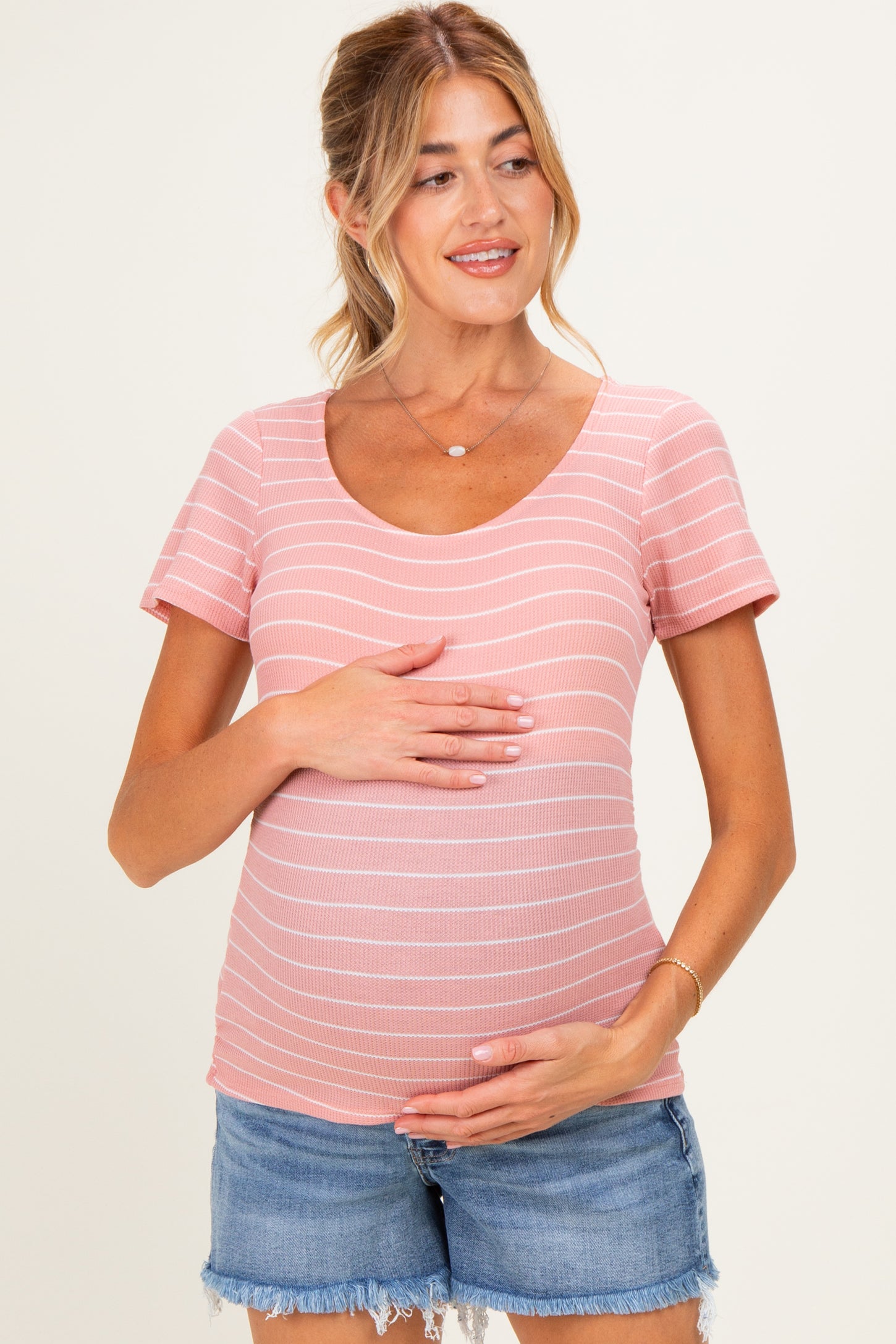 woman wearing a pink striped maternity top and holding her baby bump while smiling