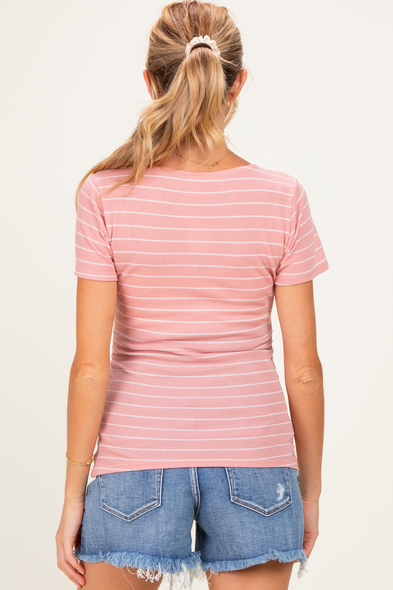 woman wearing a pink striped maternity top with a fitted style and blue denim shorts