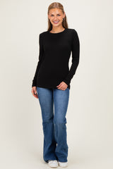 woman wearing a black long sleeve top with blue flared jeans and white sneakers, smiling at the camera
