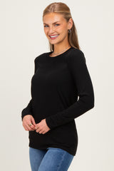 woman wearing a black long sleeve top and blue jeans, smiling at the camera