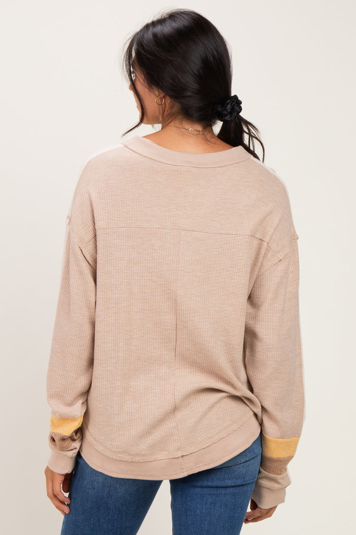 woman wearing a tan oversized long sleeve top with yellow stripe detail on the sleeves, standing backwards