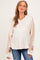 woman wearing a light beige maternity pullover with color block sleeves and a baby bump visible