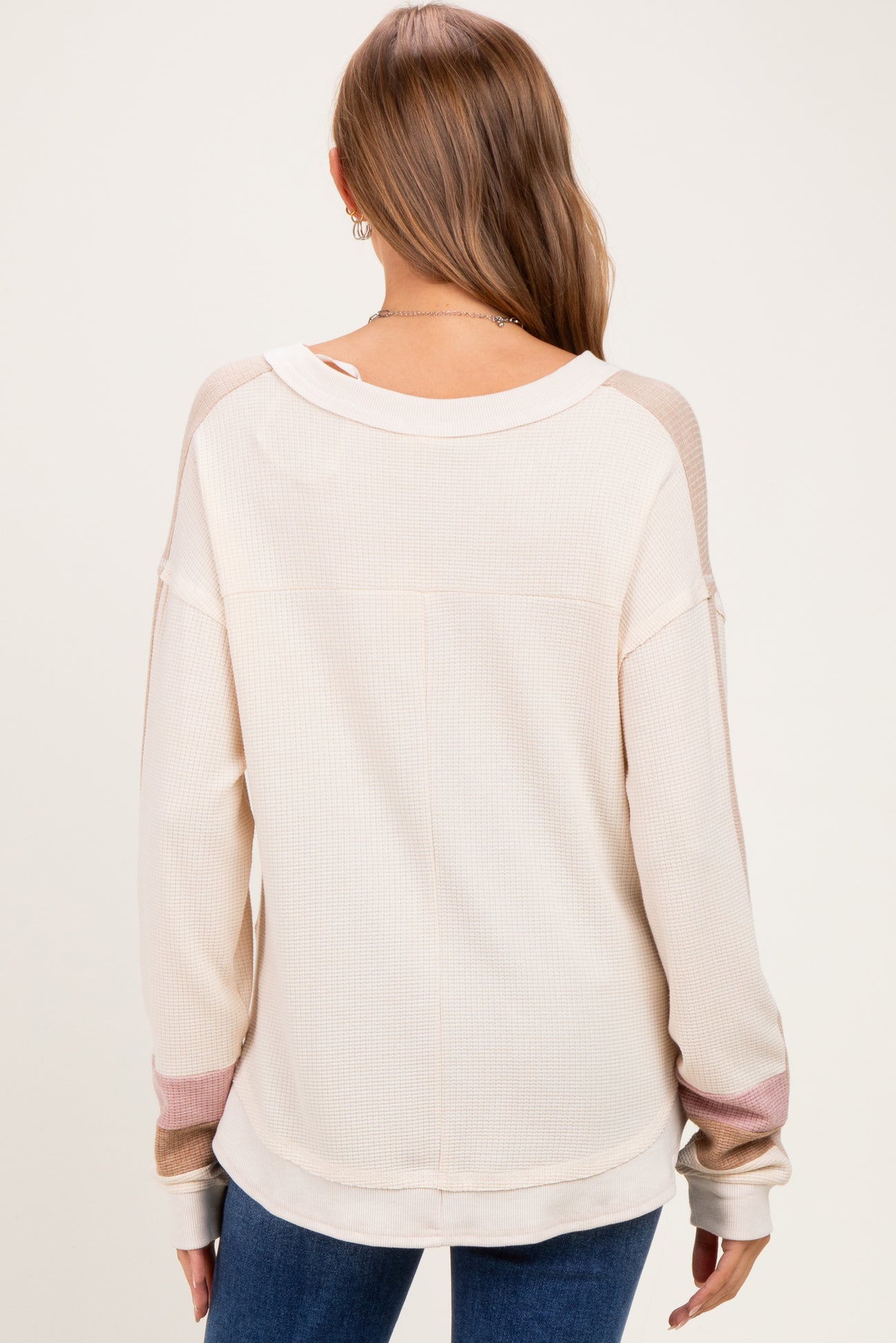 woman wearing a cream-colored long sleeve maternity top with color-blocked sleeves, showing the back view