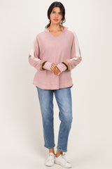 woman wearing a pink oversized hoodie with contrasting sleeves and light blue jeans, standing on a neutral background