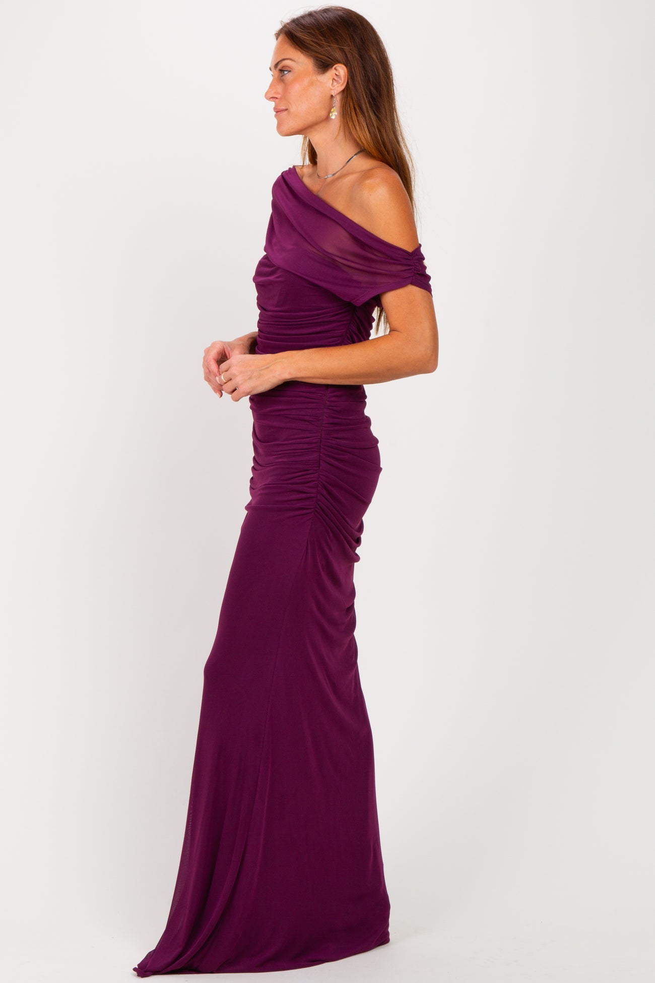 woman wearing a form-fitting off-the-shoulder purple gown with ruched detailing and a floor-length silhouette