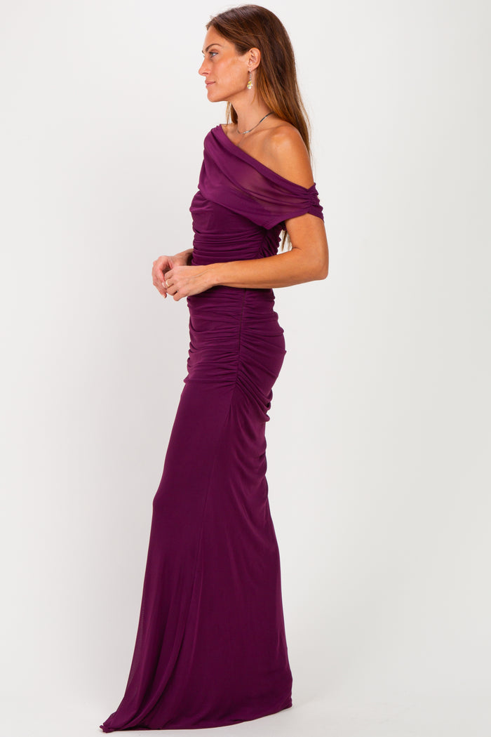 woman wearing a form-fitting off-the-shoulder purple gown with ruched detailing and a floor-length silhouette