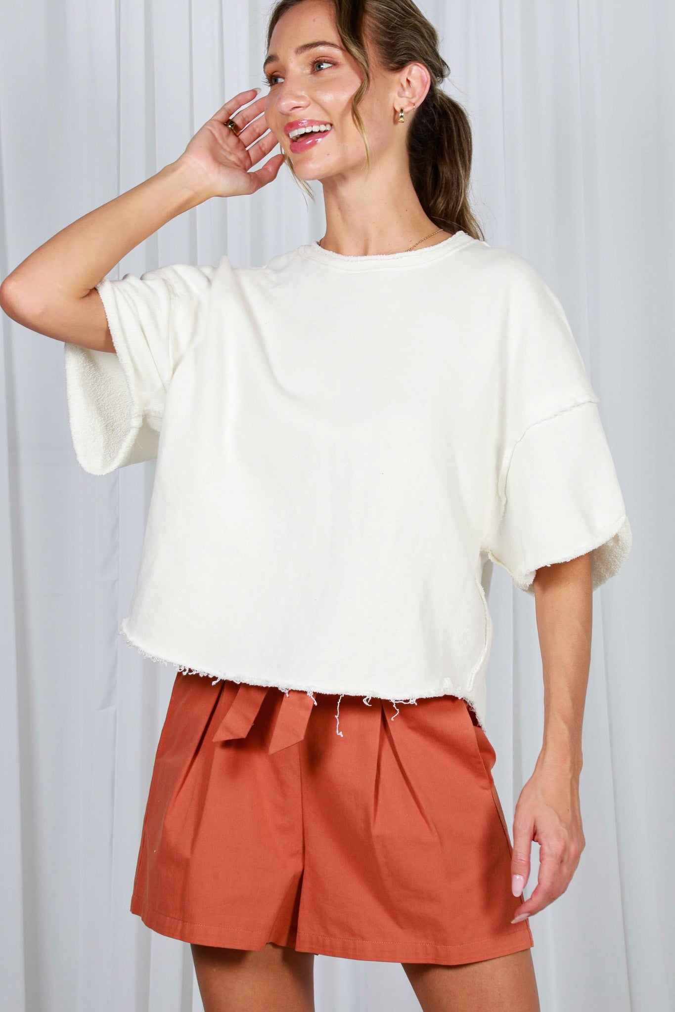 woman wearing a cream oversized t-shirt with raw hem and rust-colored pleated shorts