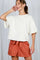 woman wearing a cream oversized t-shirt with raw hem and rust-colored pleated shorts