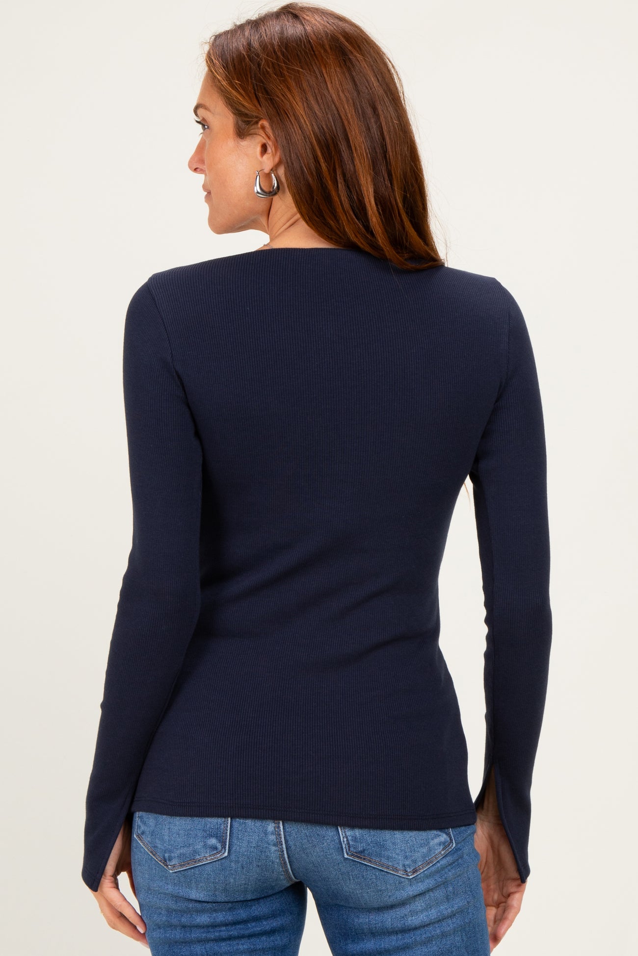 woman wearing a navy blue long sleeve ribbed top and blue jeans, showing the back view of the shirt