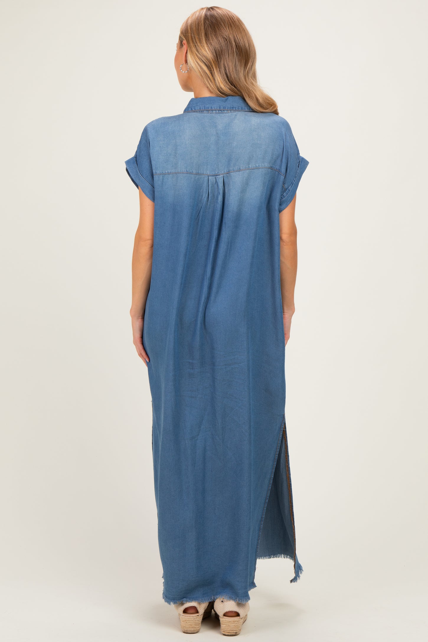 woman wearing a long denim shirt dress with short sleeves and high side slits, showing the back view