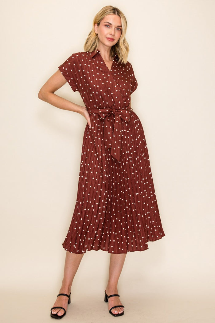 woman wearing a burgundy short sleeve collared dress with white polka dots and a tie belt, model standing in a relaxed pose