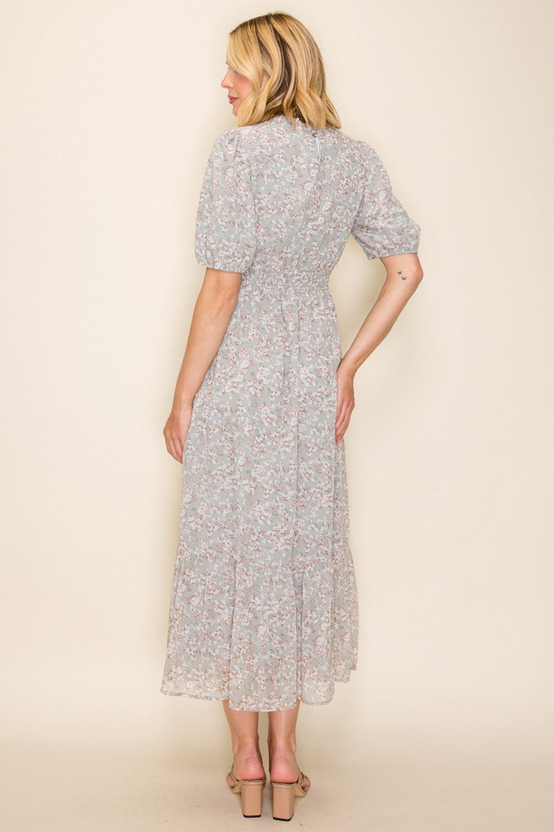 woman wearing a light floral midi dress with puff sleeves and a fitted waist, standing with her back to the camera