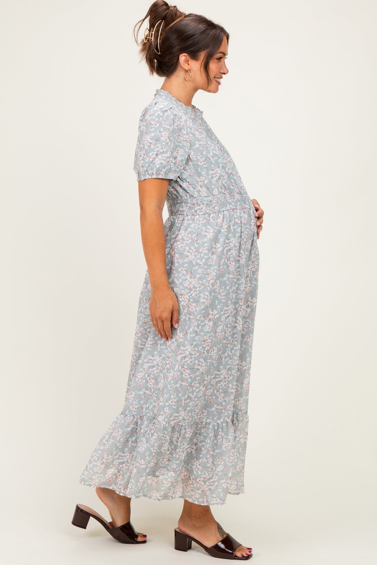 woman wearing a light blue floral maternity maxi dress with short sleeves and a gathered waist, holding her baby bump