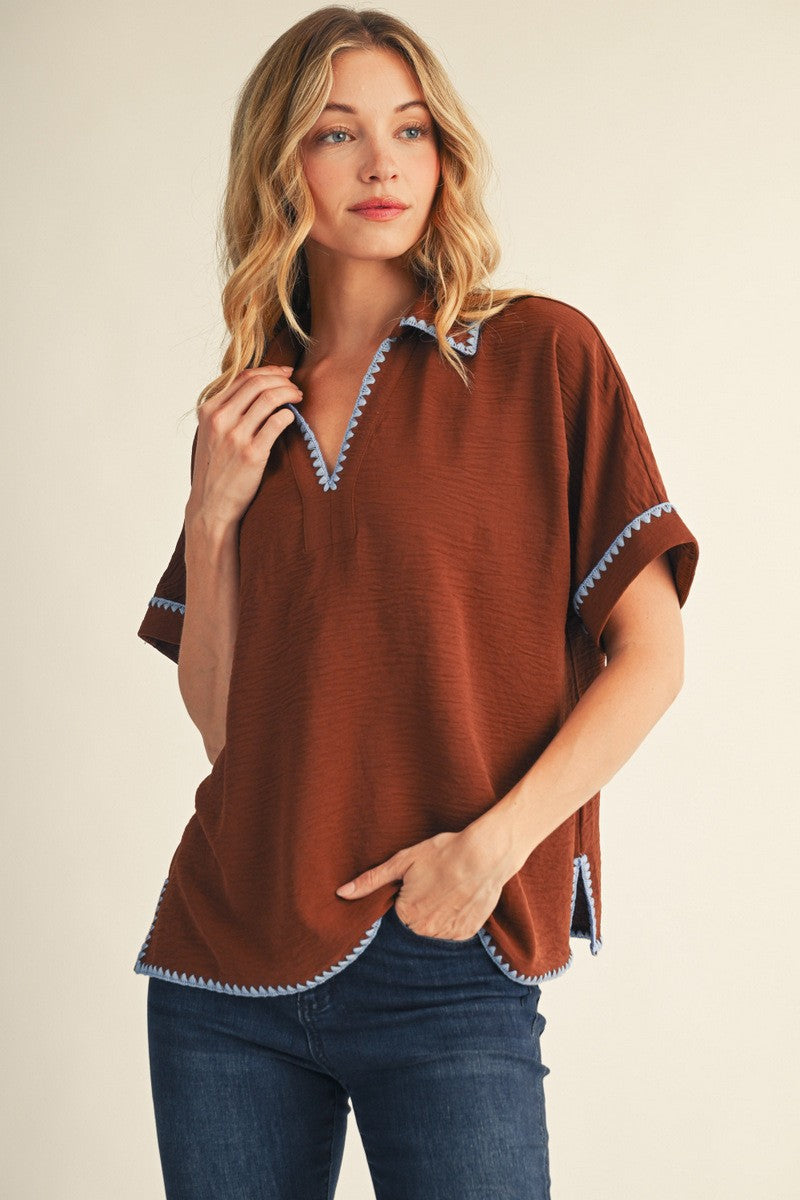 woman wearing a brown short sleeve top with blue trim and a v-neckline, paired with dark jeans