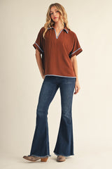 woman wearing a brown short sleeve top with contrasting collar and trim, paired with dark blue flared jeans