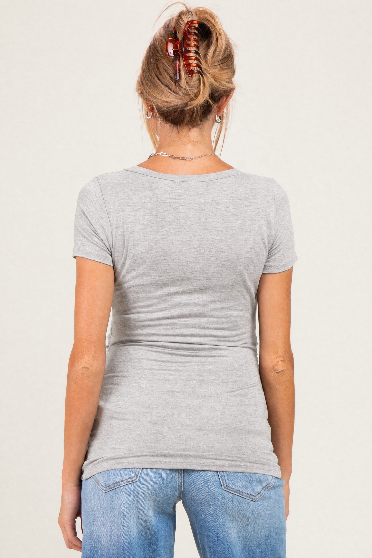woman wearing a fitted gray maternity t-shirt, viewed from the back, with casual jeans and hair in a clip